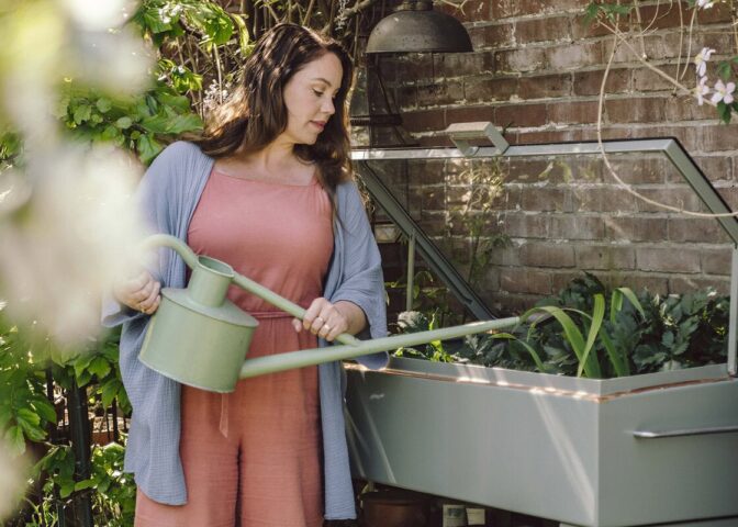 Anne geeft moestuinplanten in een kweekkas water met een gieter